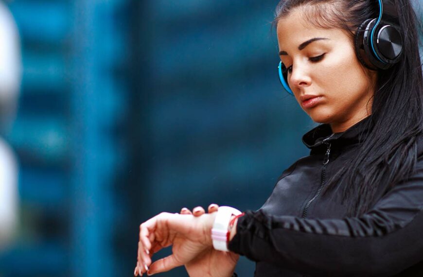 Young woman checking time at smartwatch after jogging in the city