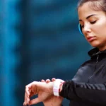 Young woman checking time at smartwatch after jogging in the city