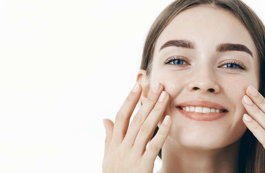 charming-relaxed-gentle-young-woman-making-cosmetological-procedure-applying-facial-cream-face-with-fingers-smiling-broadly-feeling-perfect-taking-care-skin