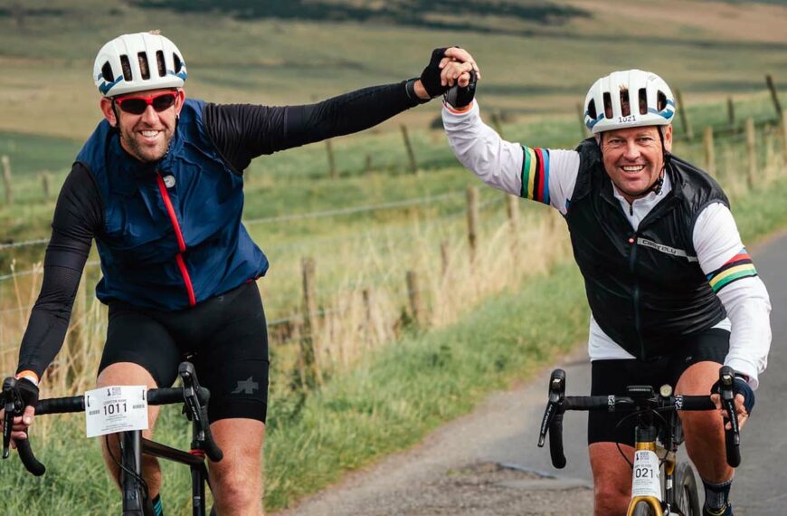 two male cyclist hold hands in celebration