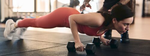 Strong sportswoman doing plank exercise with help of personal instructor