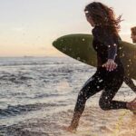 Couple is running into the water with surfboards.