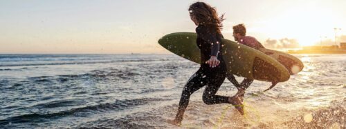 Couple is running into the water with surfboards.