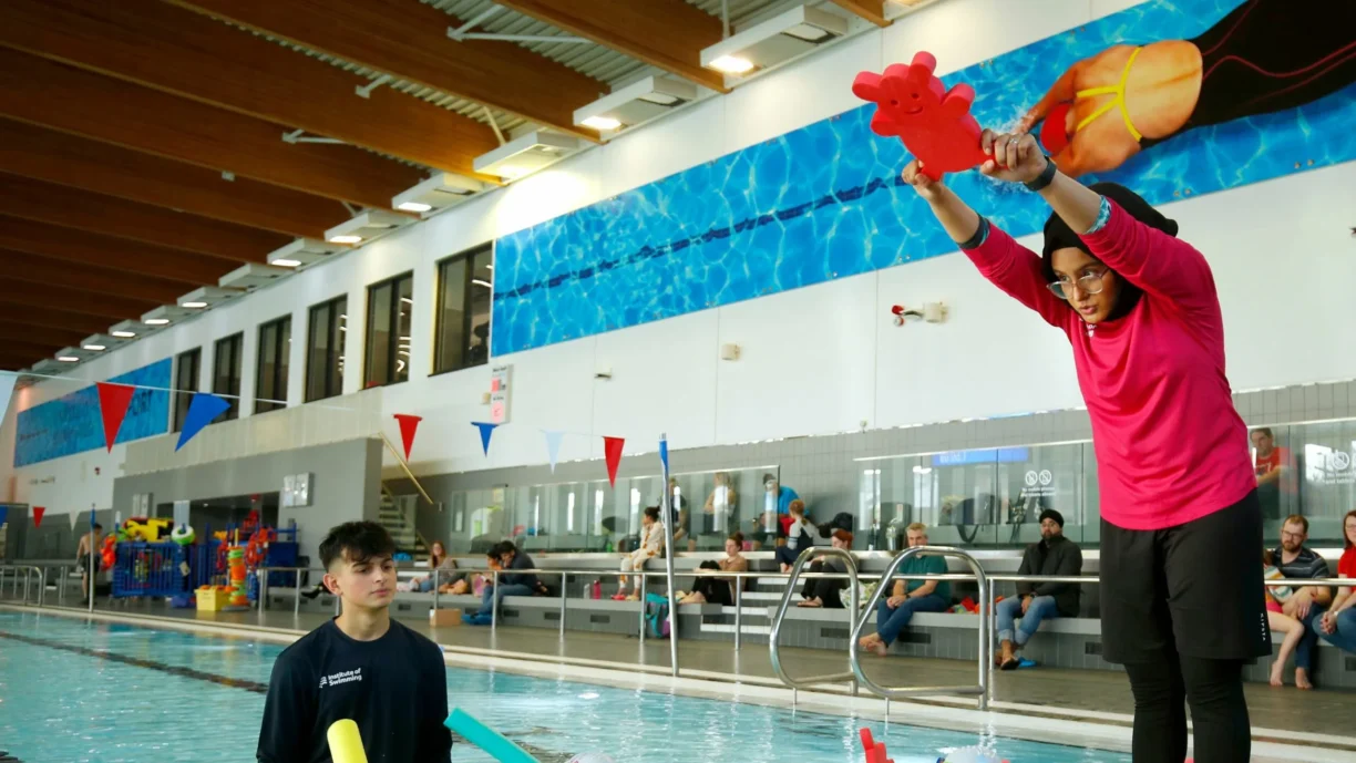 Swim-instructor-looks-on-a-young-person-practices-a-dive