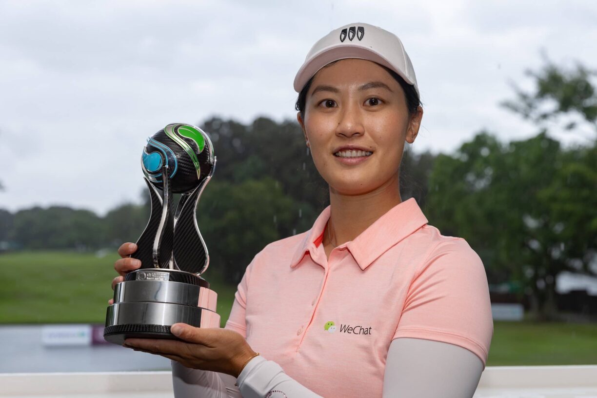 Xiyu Lin posing with the Aramco Team Series presented by PIF - Hong Kong trophy overlooking the 18th