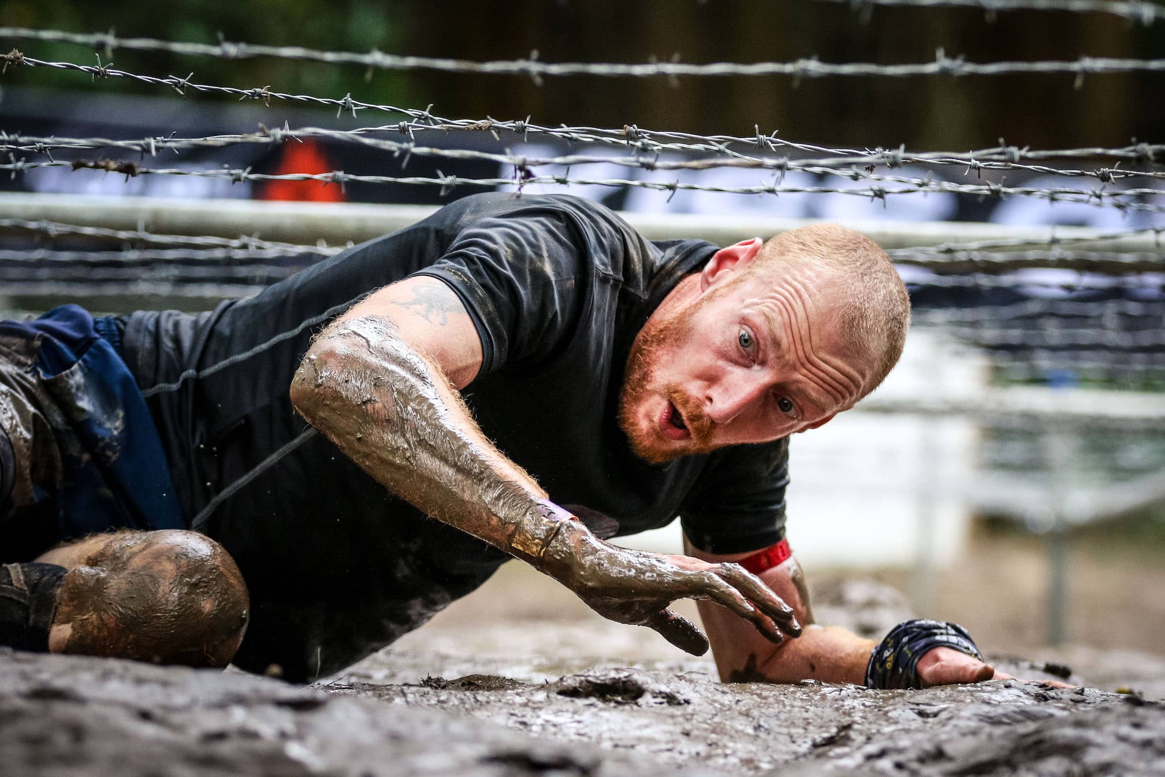 Tough Mudder Participant climbs under barbed-wire