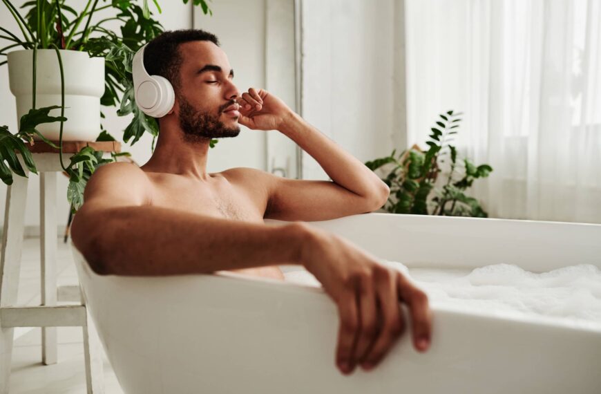 Young handsome man in wireless headphones relaxing in bath with foam and enjoying music