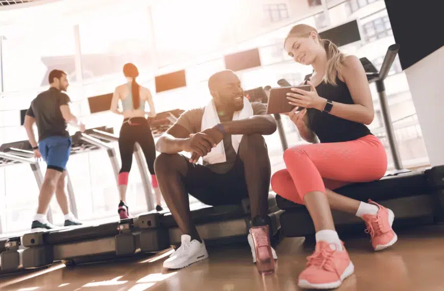 Athletes engage in modern treadmills in the bright gym. A man and a woman are sitting and talking next to the treadmills.