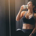 woman in sportswear drinking protein powder milkshake after workout at fitness gym