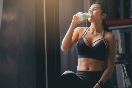 woman in sportswear drinking protein powder milkshake after workout at fitness gym