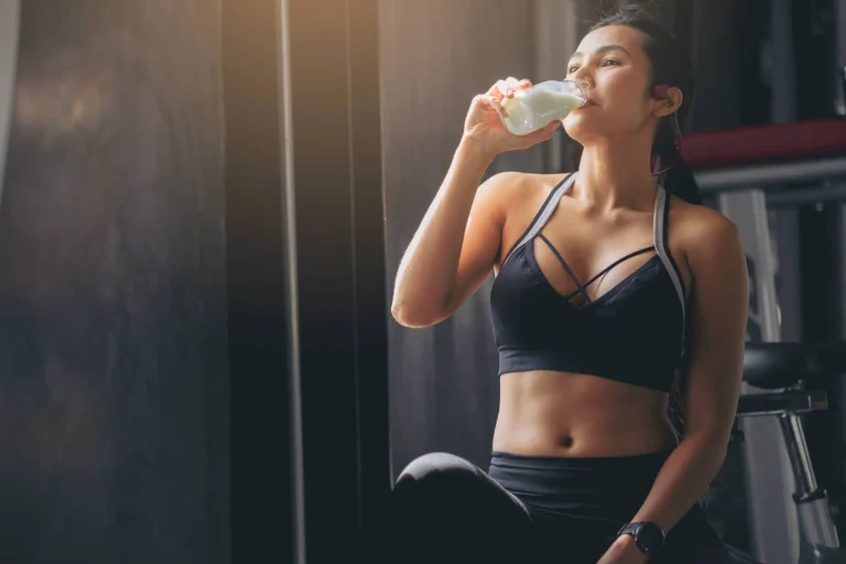 woman in sportswear drinking protein powder milkshake after workout at fitness gym