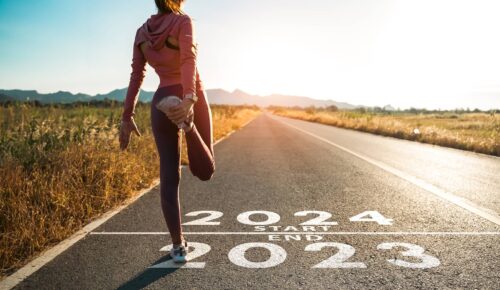 The word 2024 written on the asphalt road and athlete woman runner stretching leg preparing for new year at sunset
