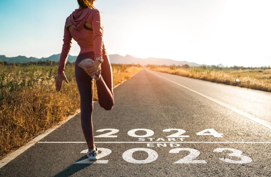 The word 2024 written on the asphalt road and athlete woman runner stretching leg preparing for new year at sunset