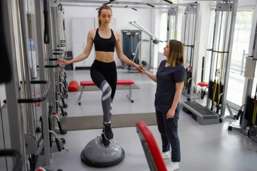 Physiotherapist helping female patient with rehabilitation. Balance exercise with bosu ball.