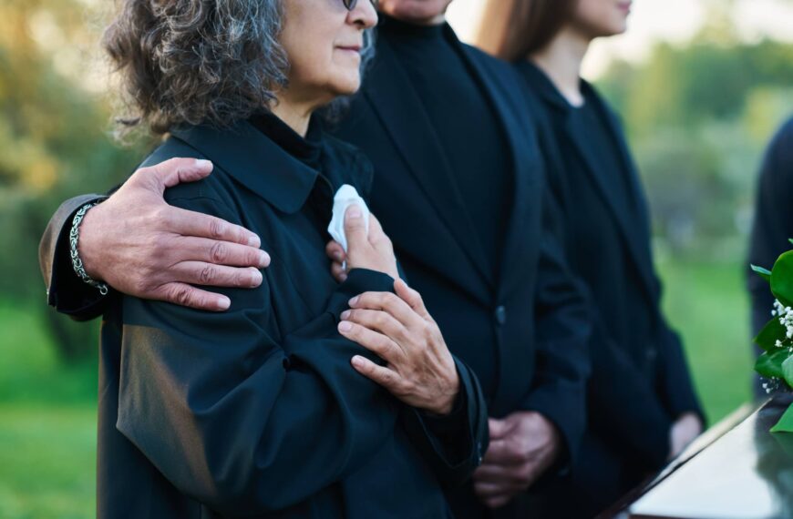 Hand of mature man on shoulder of his wife or sister with handkerchief lamenting passes away relative or family member during funeral service