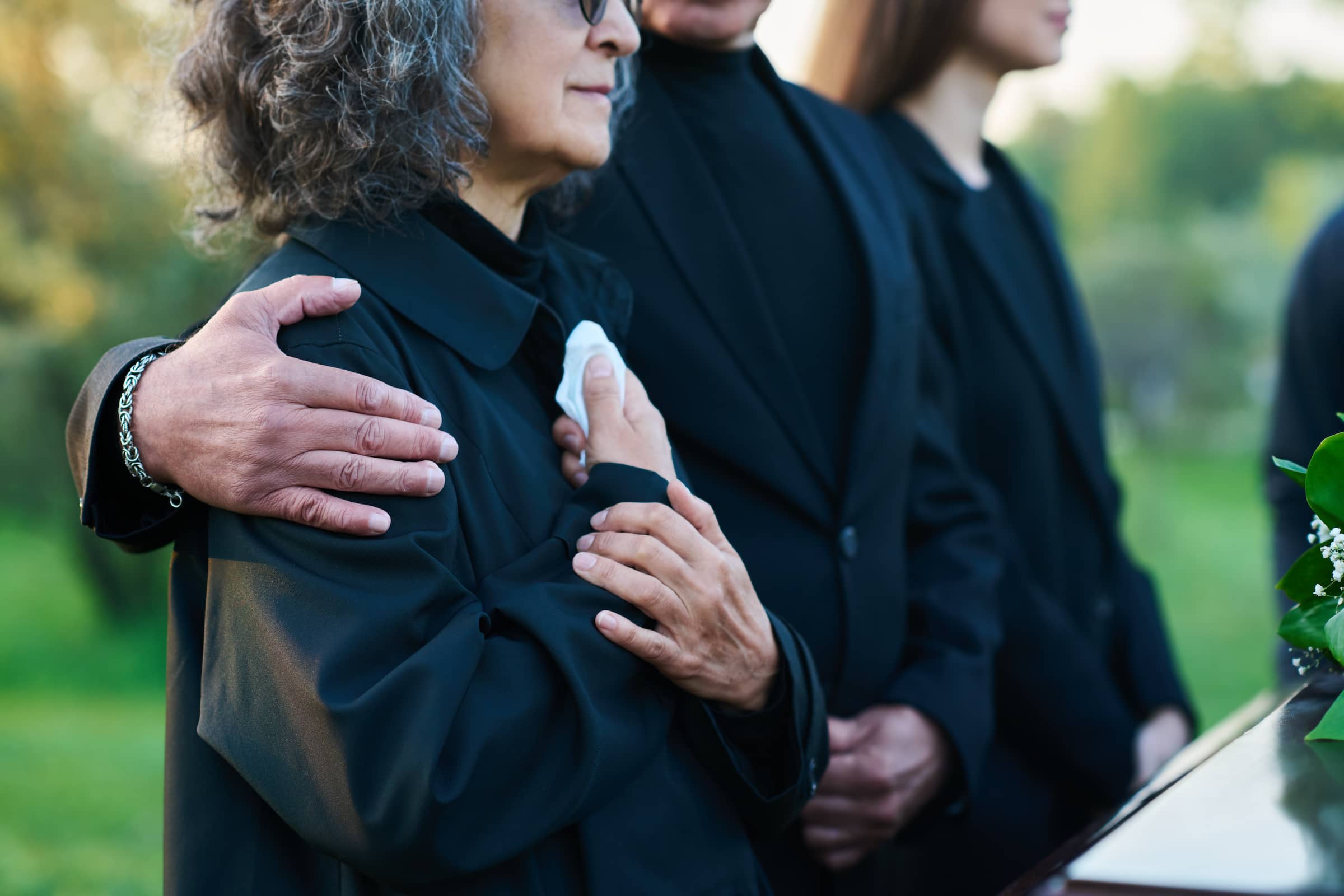 Hand of mature man on shoulder of his wife or sister with handkerchief lamenting passes away relative or family member during funeral service