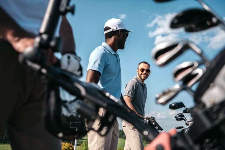 Smiling players going to the golf course, bag with clubs at foreground