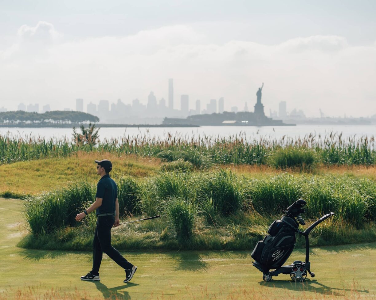 Stewart Golf Trolley being used on golf course with statue of liberty in background