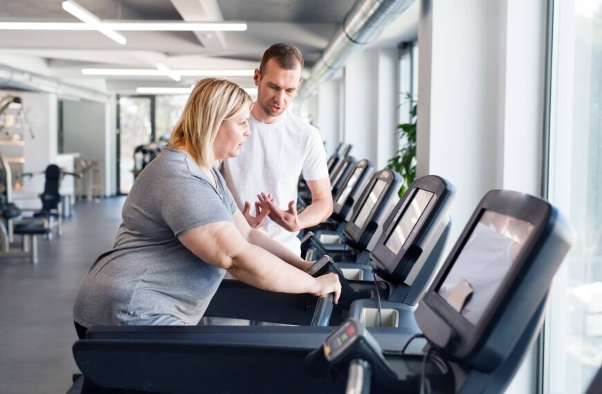 Overweight woman exercising on treadmill in gym. Personal trainer helping her.