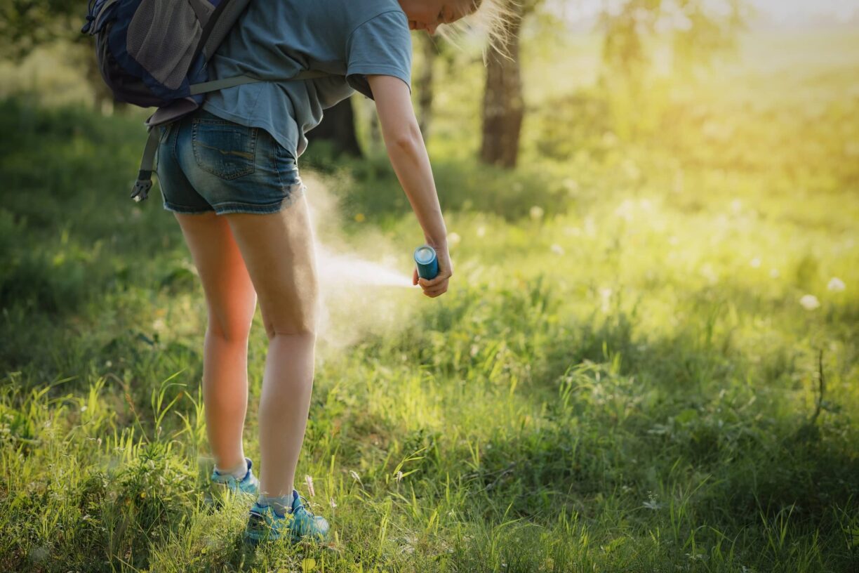 Hiker applying mosquito repellent on the leg skin in the forest.