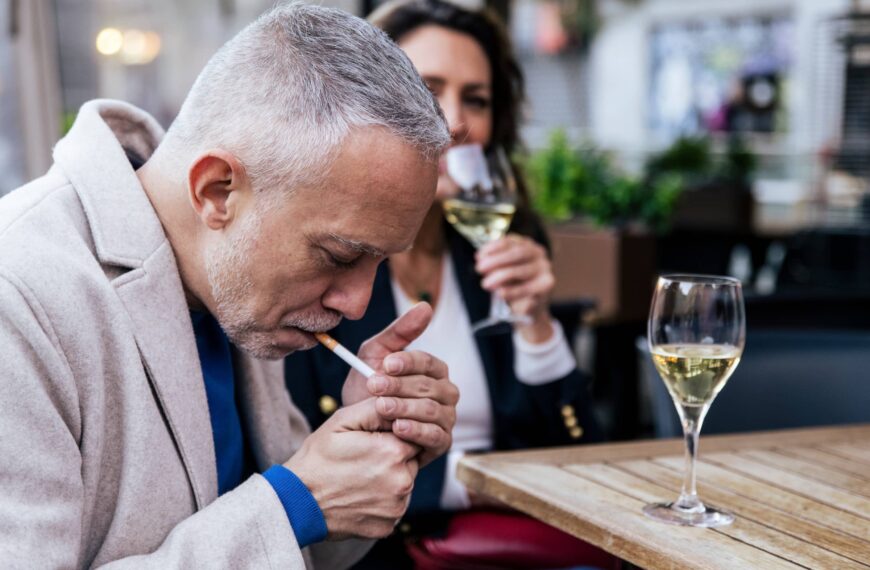 Middle aged man smoking tobacco and drinking wine in a terrace with a woman