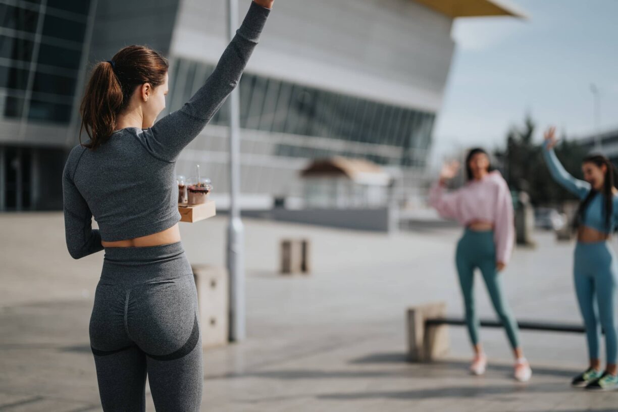 Woman in fitness attire greeting friends in urban setting, showcasing active lifestyle and friendship