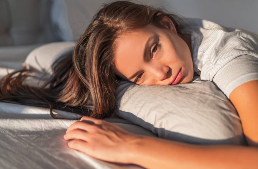 young person waking up in bed sleepy morning fatigue with half open eyes