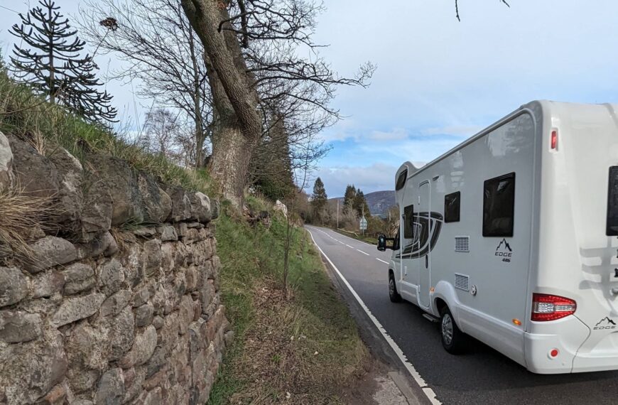 A road with a caravan driving down it and little space for anyone to walk safely