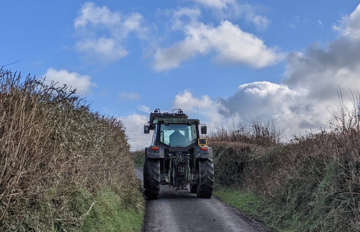 A tractor driving down a narrow lane with no space for any walkers