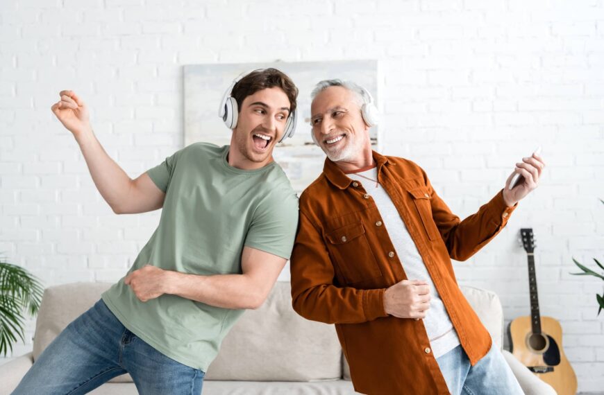 Person in wireless headphones singing and dancing with mature and cheerful person at home