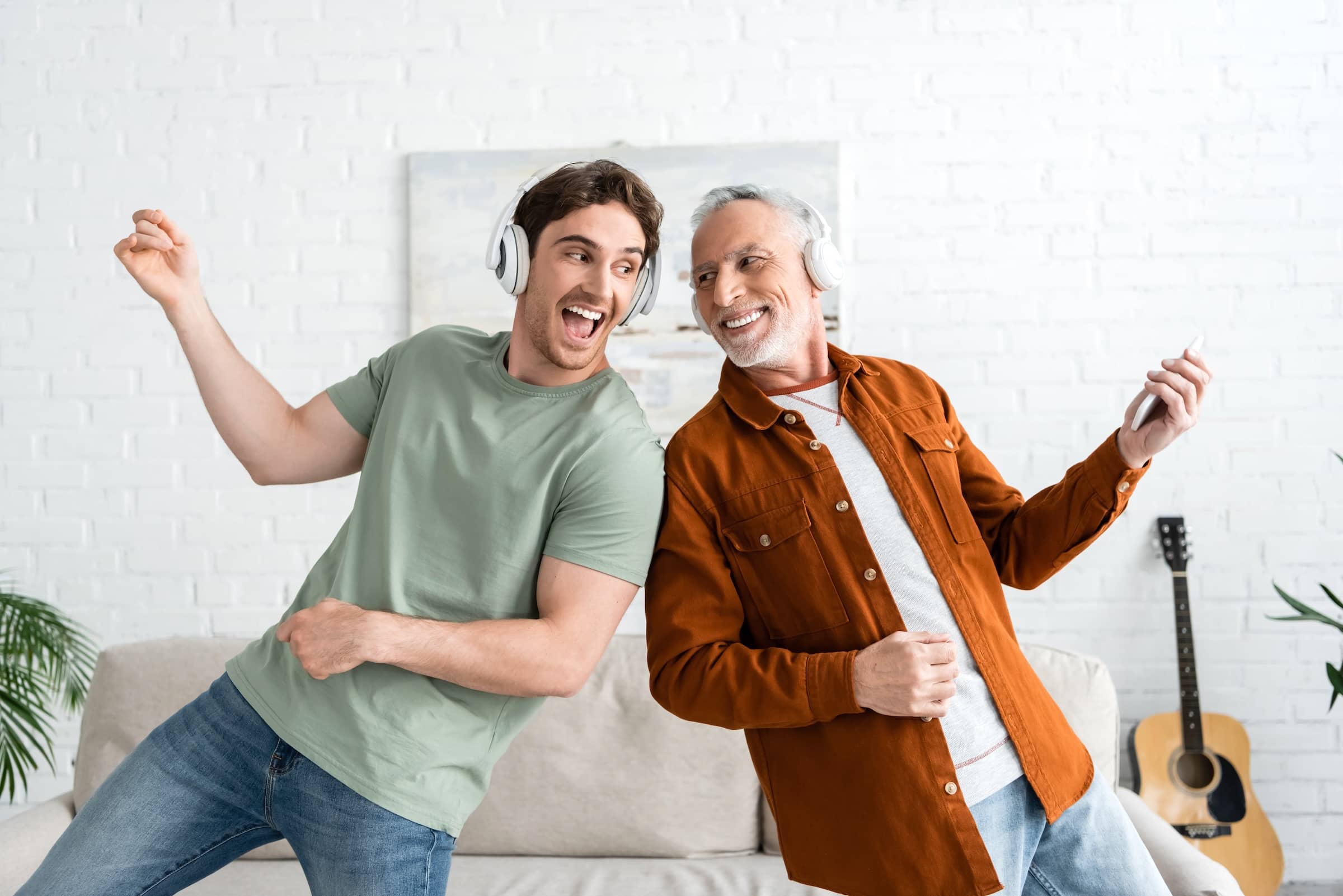 Person in wireless headphones singing and dancing with mature and cheerful person at home