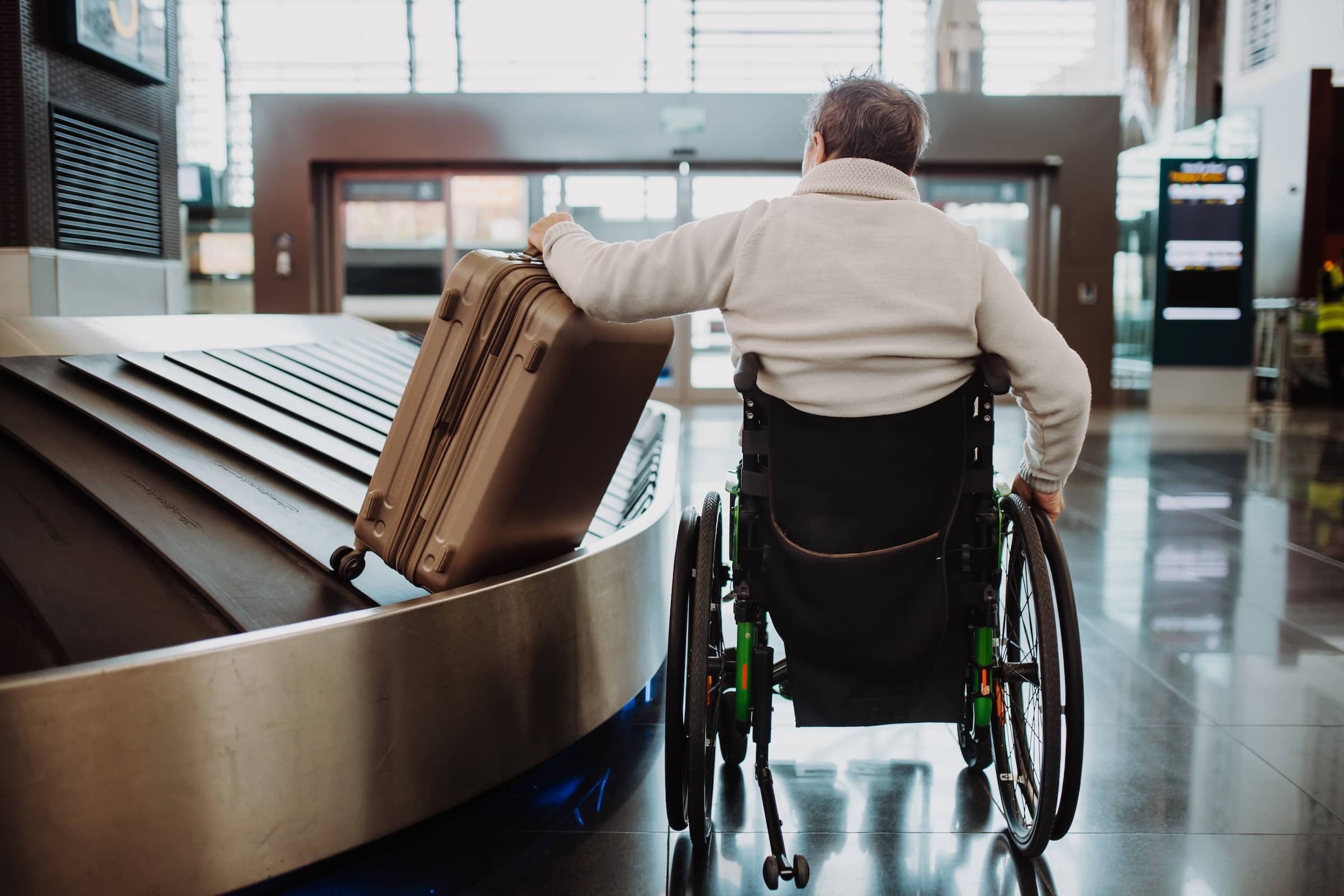 Rear view of man on wheelchair at airport with his luggage