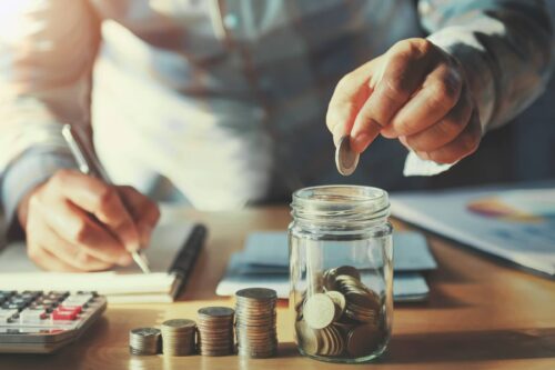 Saving money concept. hand holding coins putting in jug glass