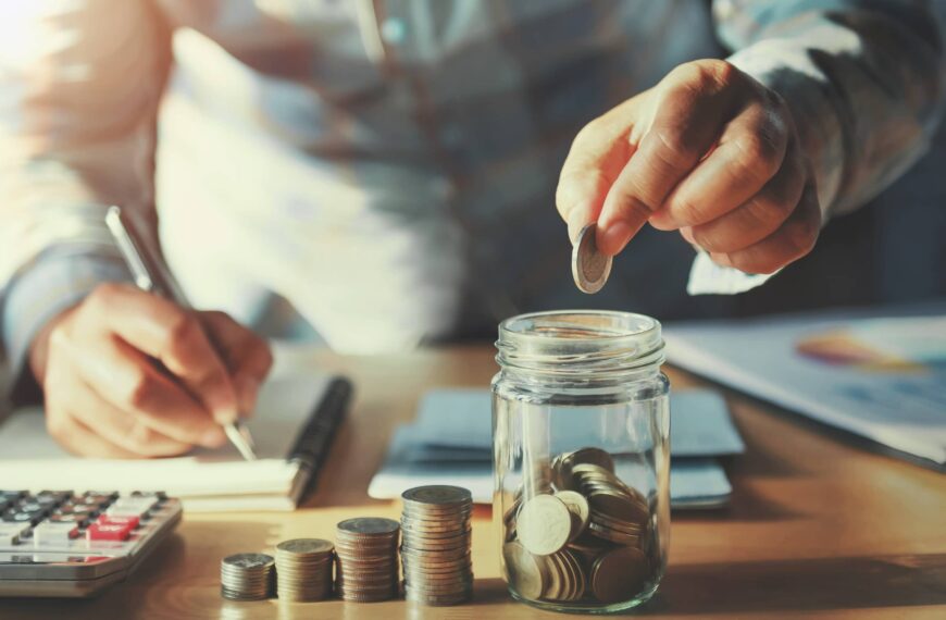 Saving money concept. hand holding coins putting in jug glass