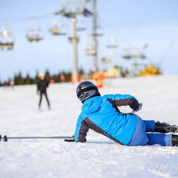 Skier in blue ski suit after the fall on mountain slope trying get up against ski-lift.