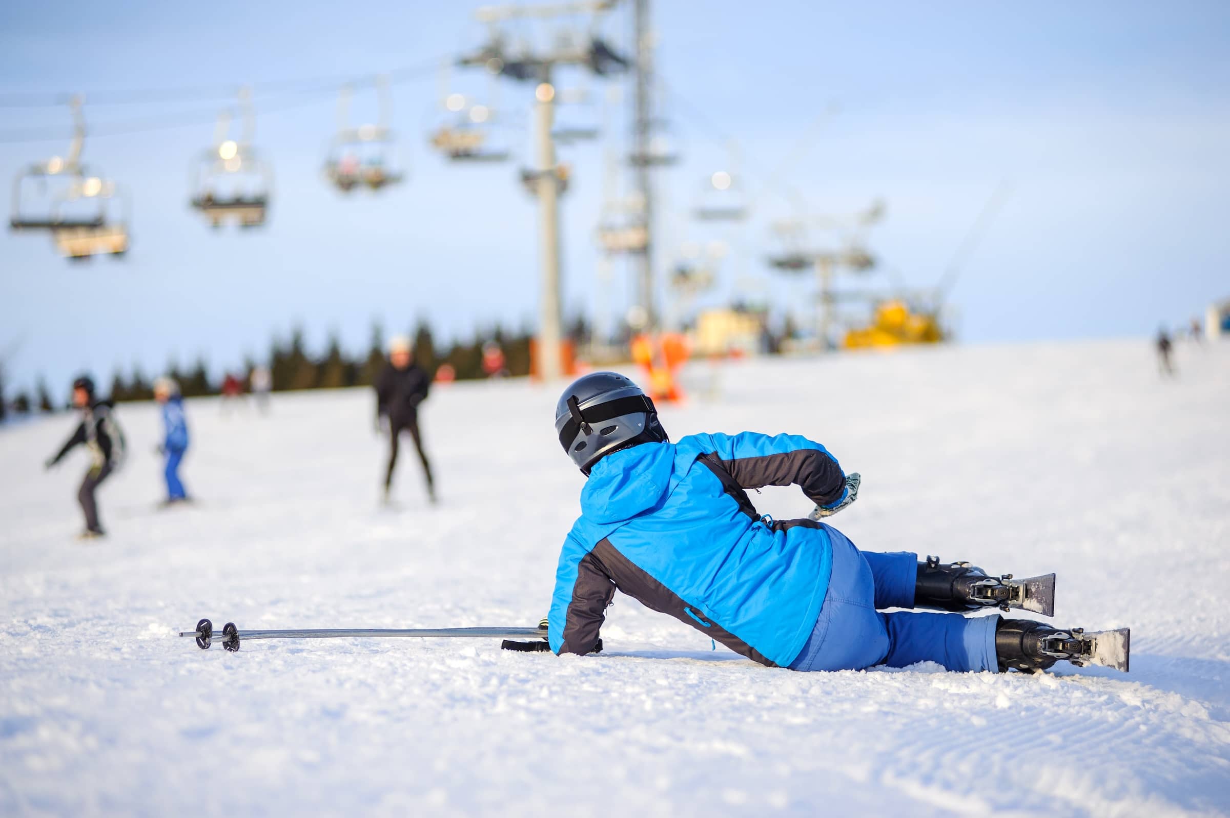 Skier in blue ski suit after the fall on mountain slope trying get up against ski-lift.