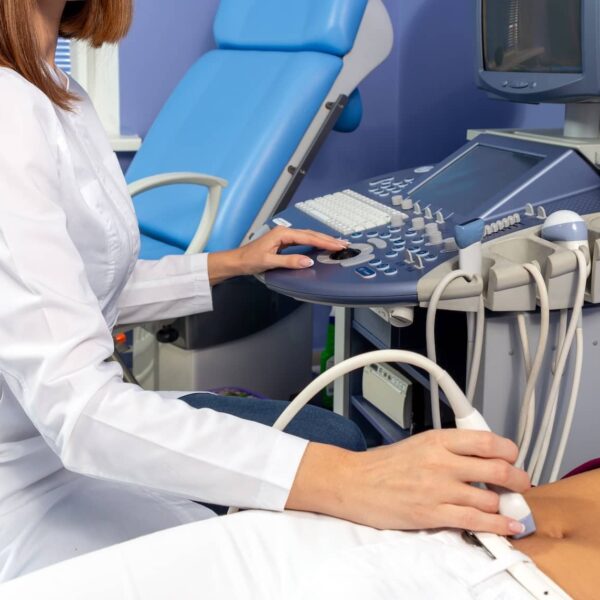 The doctor performs an ultrasound diagnosis of the abdominal cavity of a pregnant girl at an early stage of pregnancy.