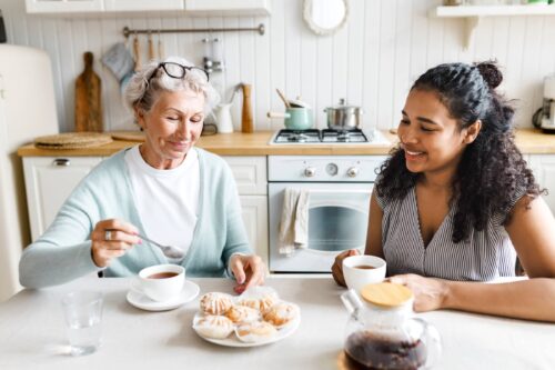 Young woman drinking tea with elderly person treating her with lunchtime tea