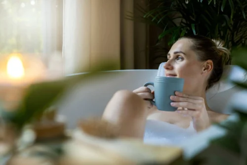 woman relaxing in bath and drink a coffee at home bathroom. looking out of window