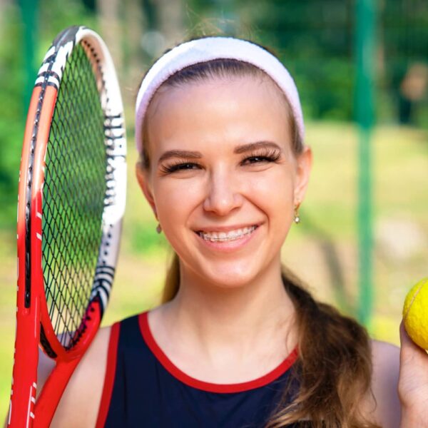 Woman smiles with tennis ball and racket in hand