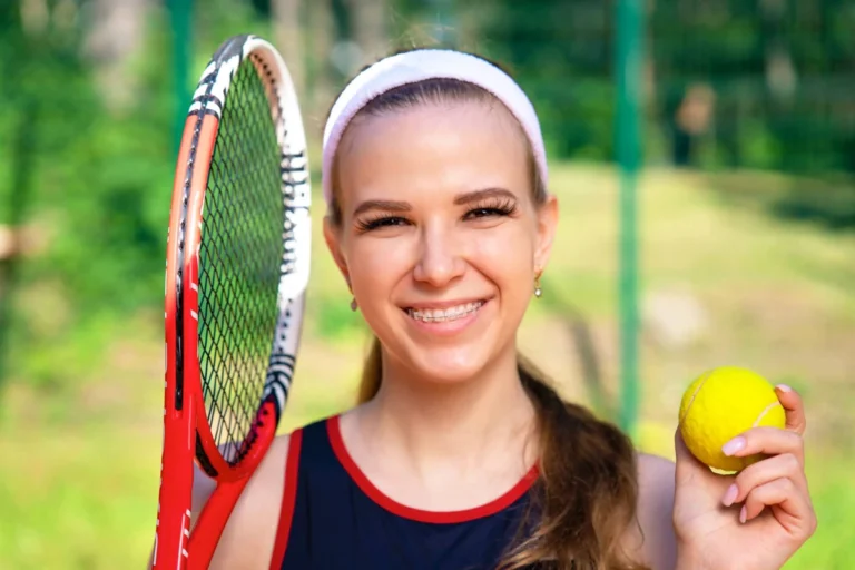 Woman smiles with tennis ball and racket in hand