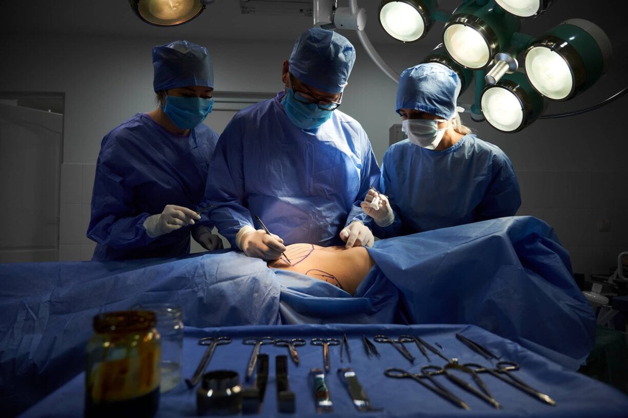 Group of doctors in sterile gloves and protective face masks doing cosmetic surgery in operating room at hospital