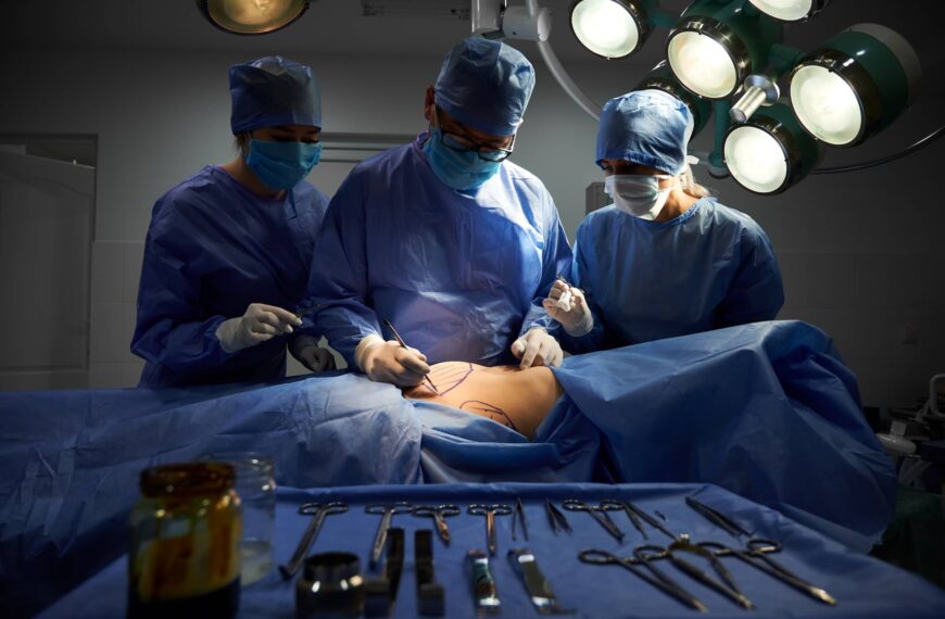 Group of doctors in sterile gloves and protective face masks doing cosmetic surgery in operating room at hospital