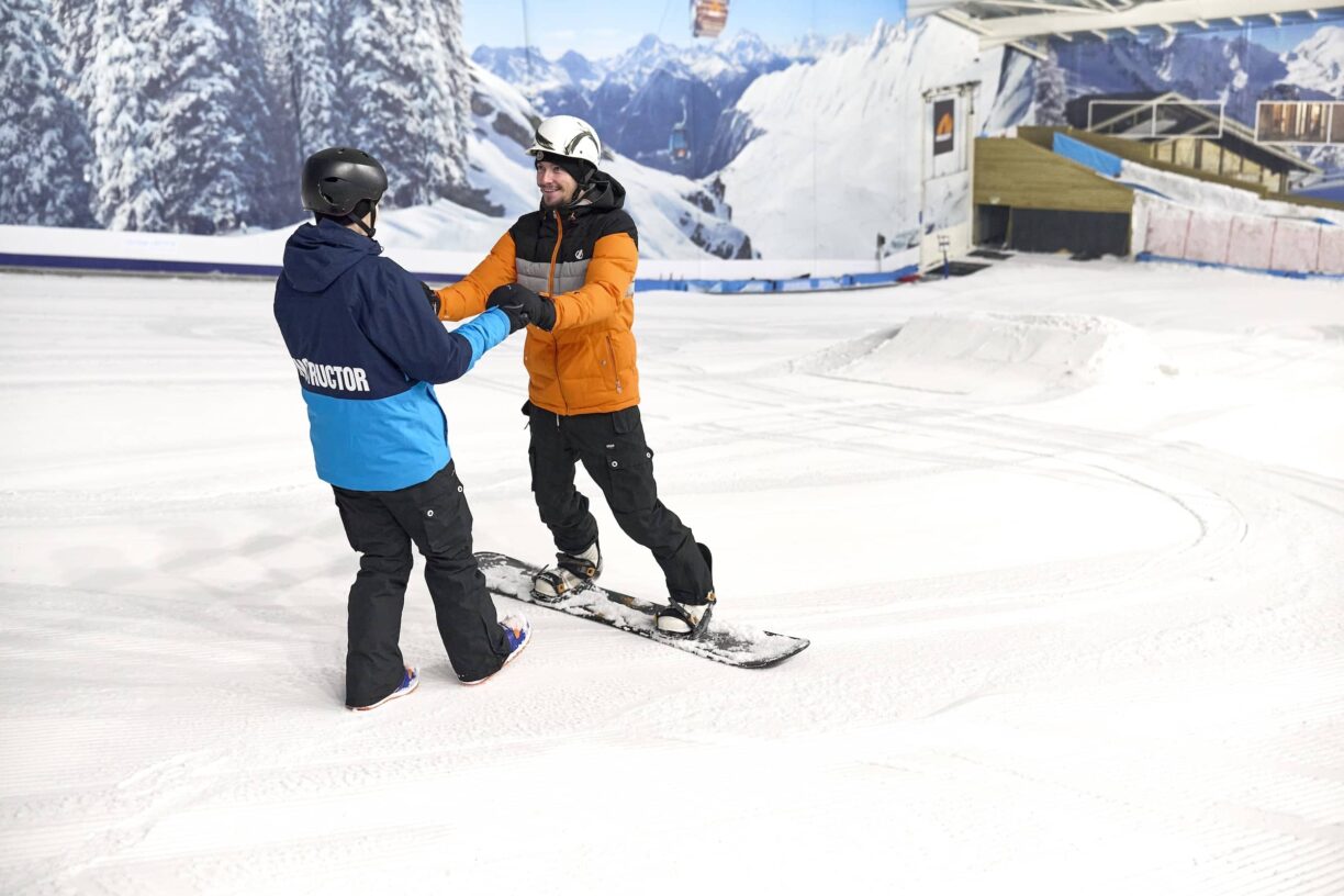 Instructor helps person on snowboard