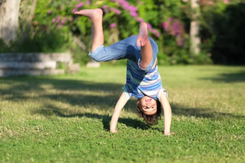 Mischievous preschooler boy somersaults on sand grass in the park
