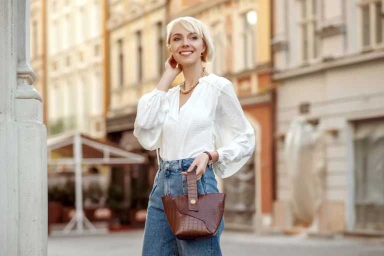 Street style photo of elegant fashionable woman wearing trendy white blouse, high waist jeans, wrist watch