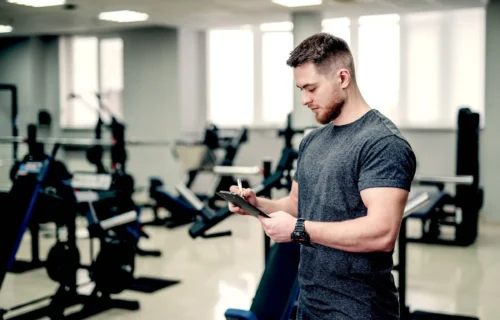 Trainer looking at fitness plan on clipboard for working out in the fitness gym