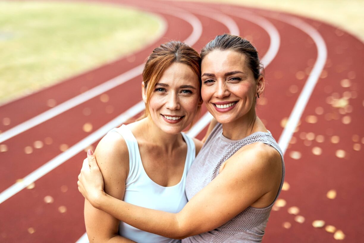Two Friends Embracing Happily On A Stadium Running Track
