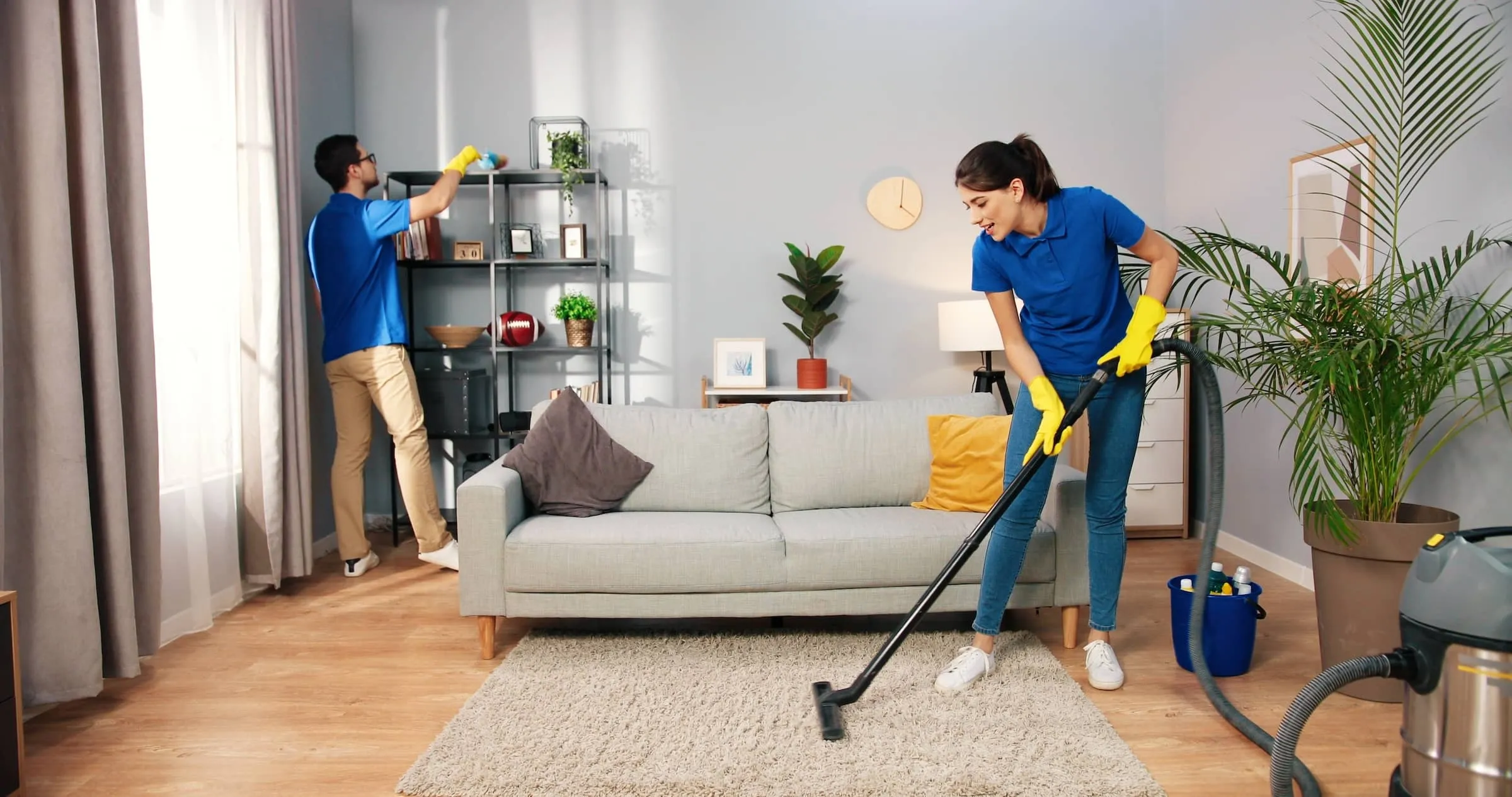 woman in yellow gloves vacuuming carpet floor at home in living room.
