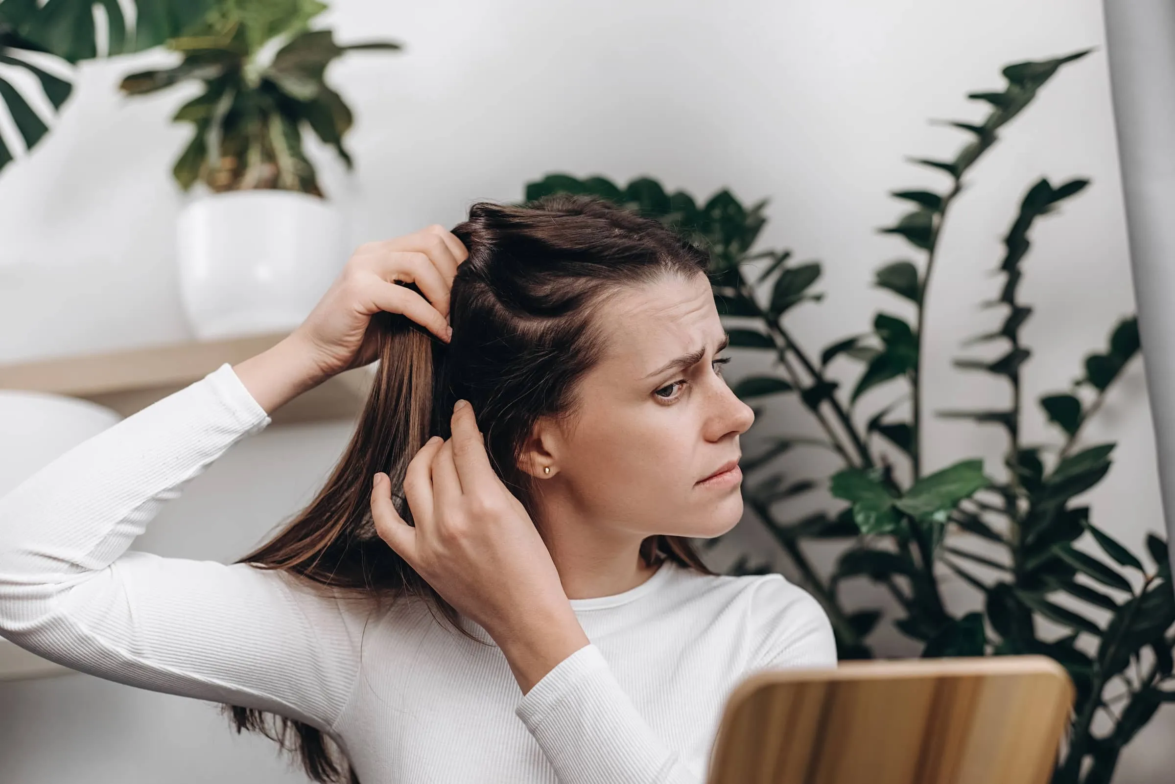 young woman sit on sofa looking in mirror with scared nervous expression as she notices bad signs like scalp